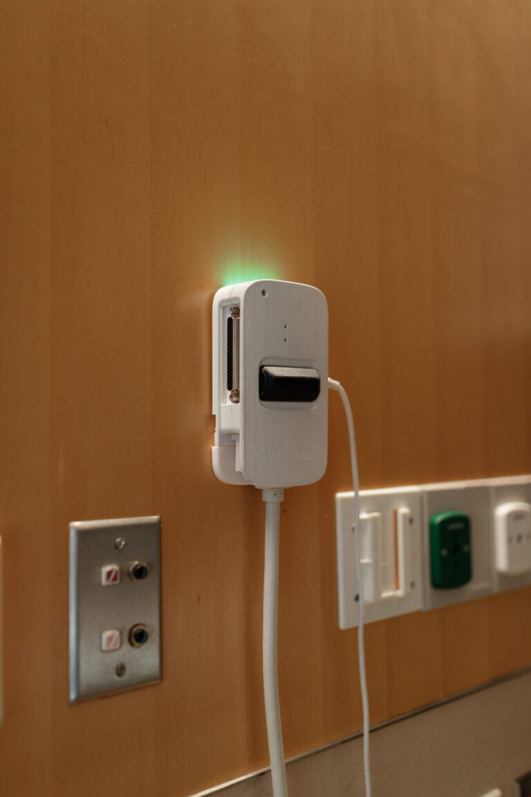 A BlueJack wall unit with a green light, mounted beside the patient station.