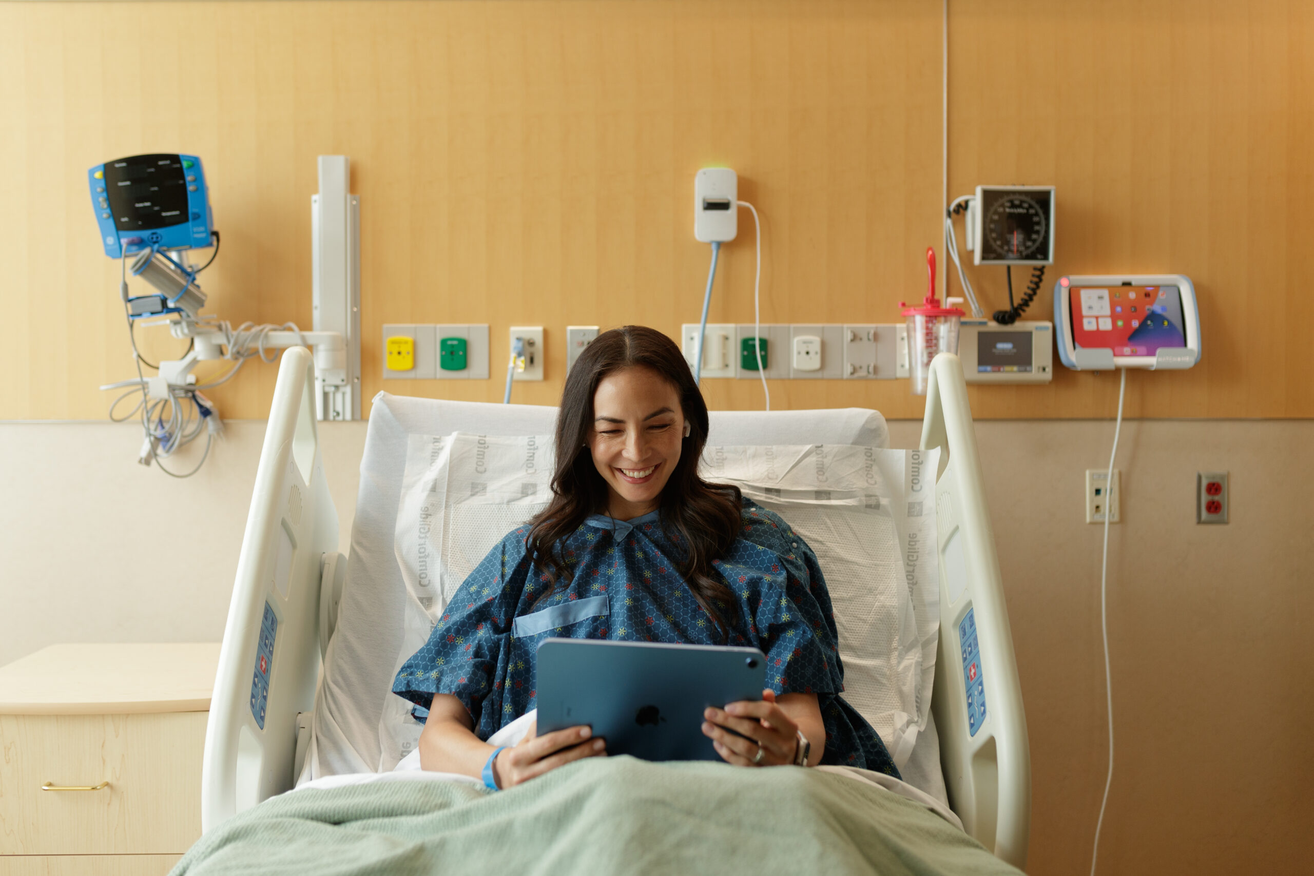 Patient resting in a hospital bed with HatchMed HallMonitor digital door signage displayed outside the patient room during a hospital renovation project.