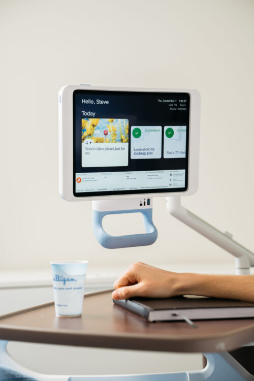 An iPad in a PadLock enclosure on a mounted arm above a bedside table.
