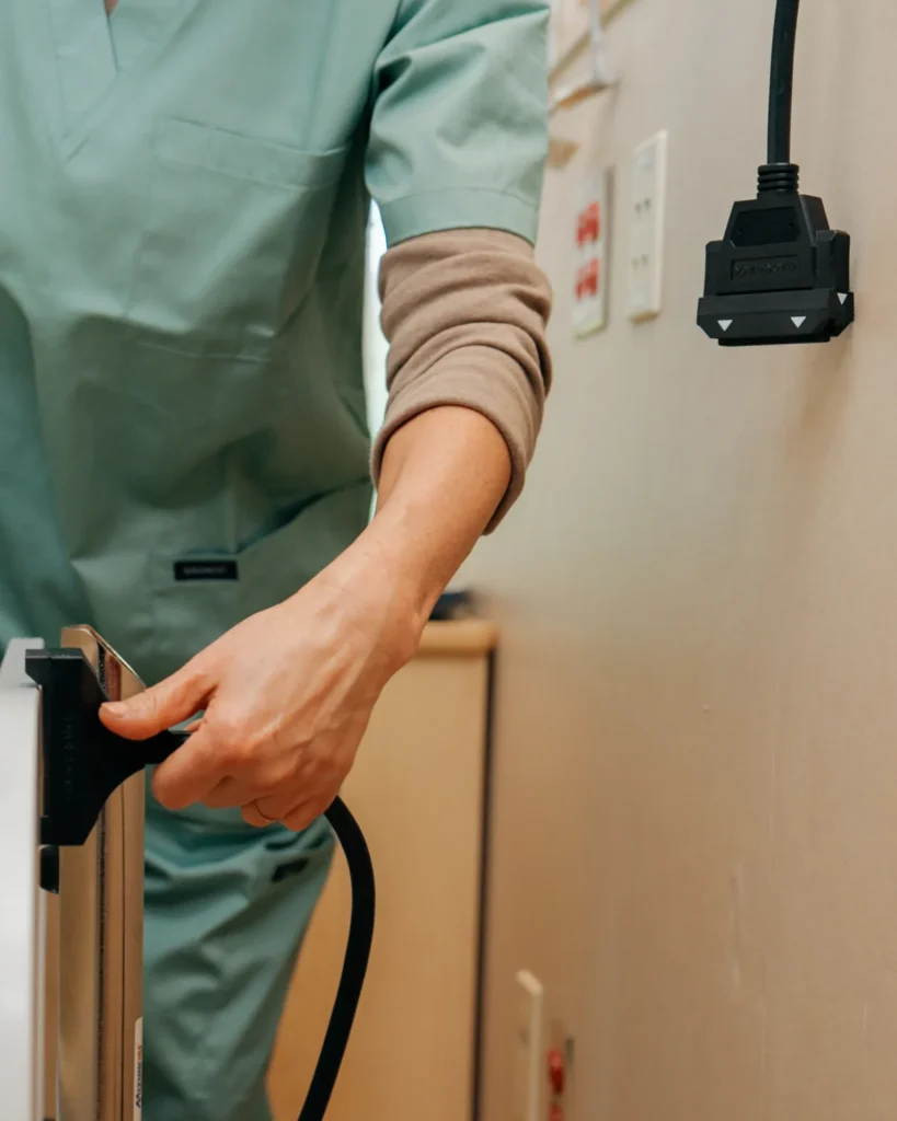 A nurse plugs a BlackJack cable into a hospital bed, with the magnetic wall end mounted on the headwall above.