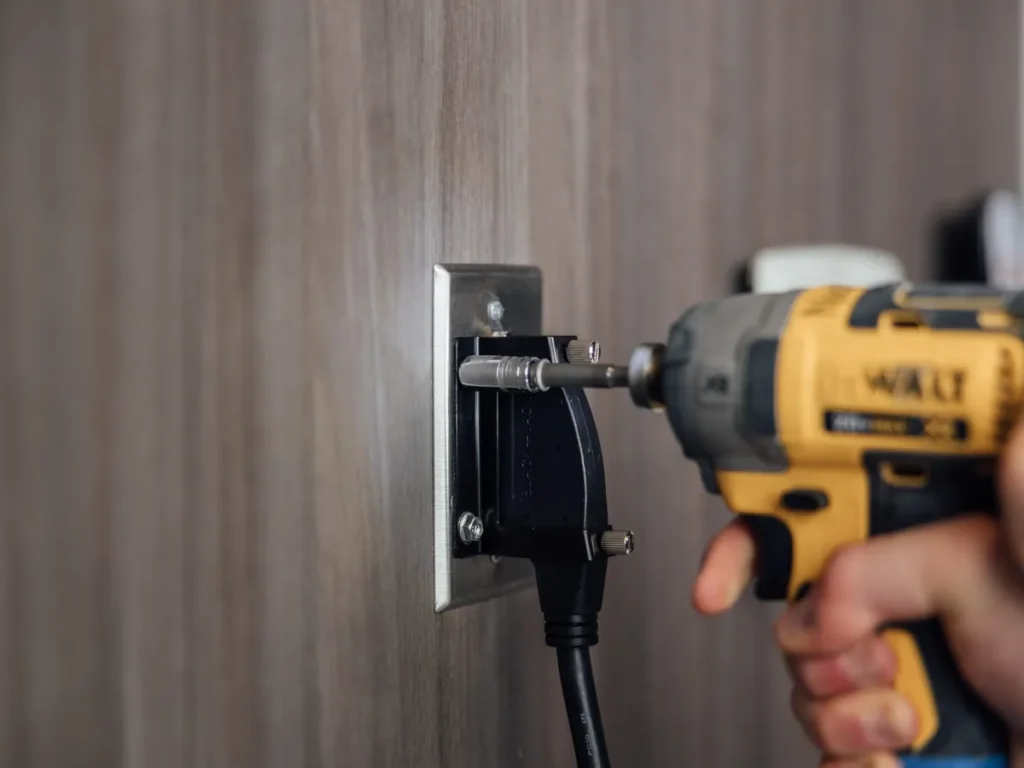 A drill drives the mounting screw on a BlackJack wall plate, with the cable connected.