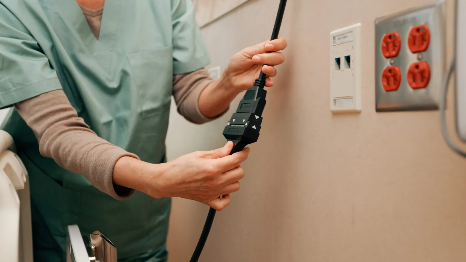 A nurse holds a BlackJack magnetic connector at the nurse call jack in a patient room.