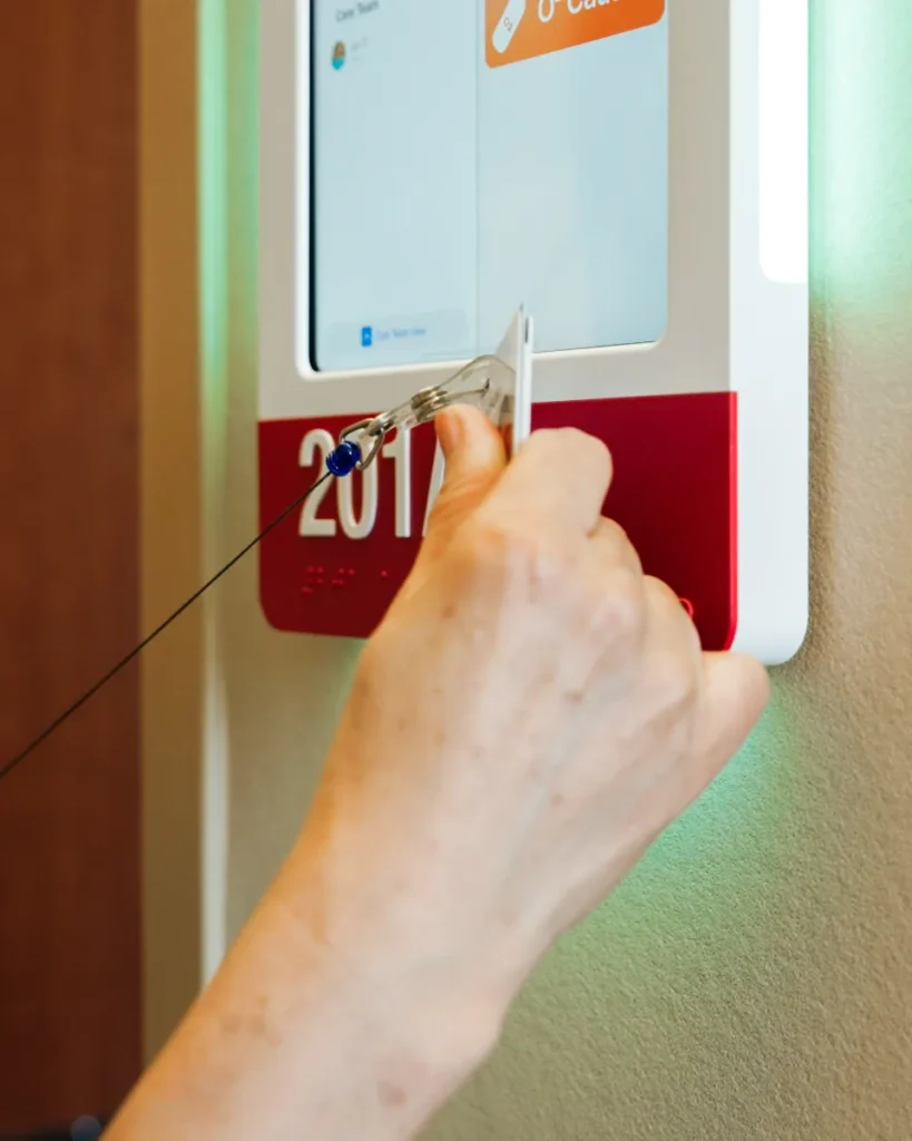 A nurse holds a badge on a retractable reel to a HallMonitor lit soft green.