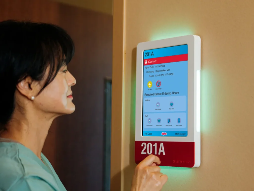 A nurse reads Epic Monitor's Room Display on a HallMonitor outside room 201A, its side panels lit green.