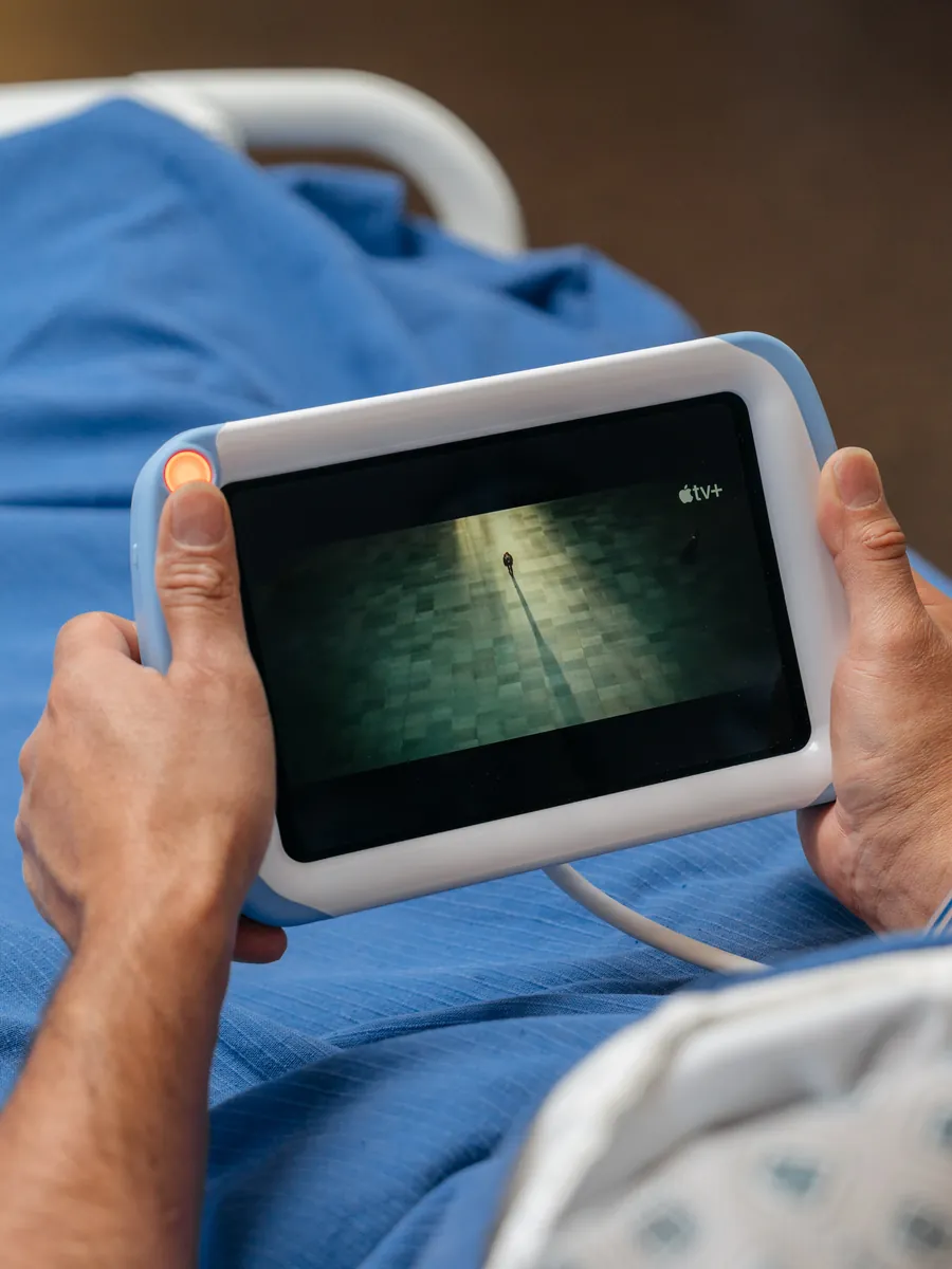 A patient holds a PillowCase in bed, watching a video.
