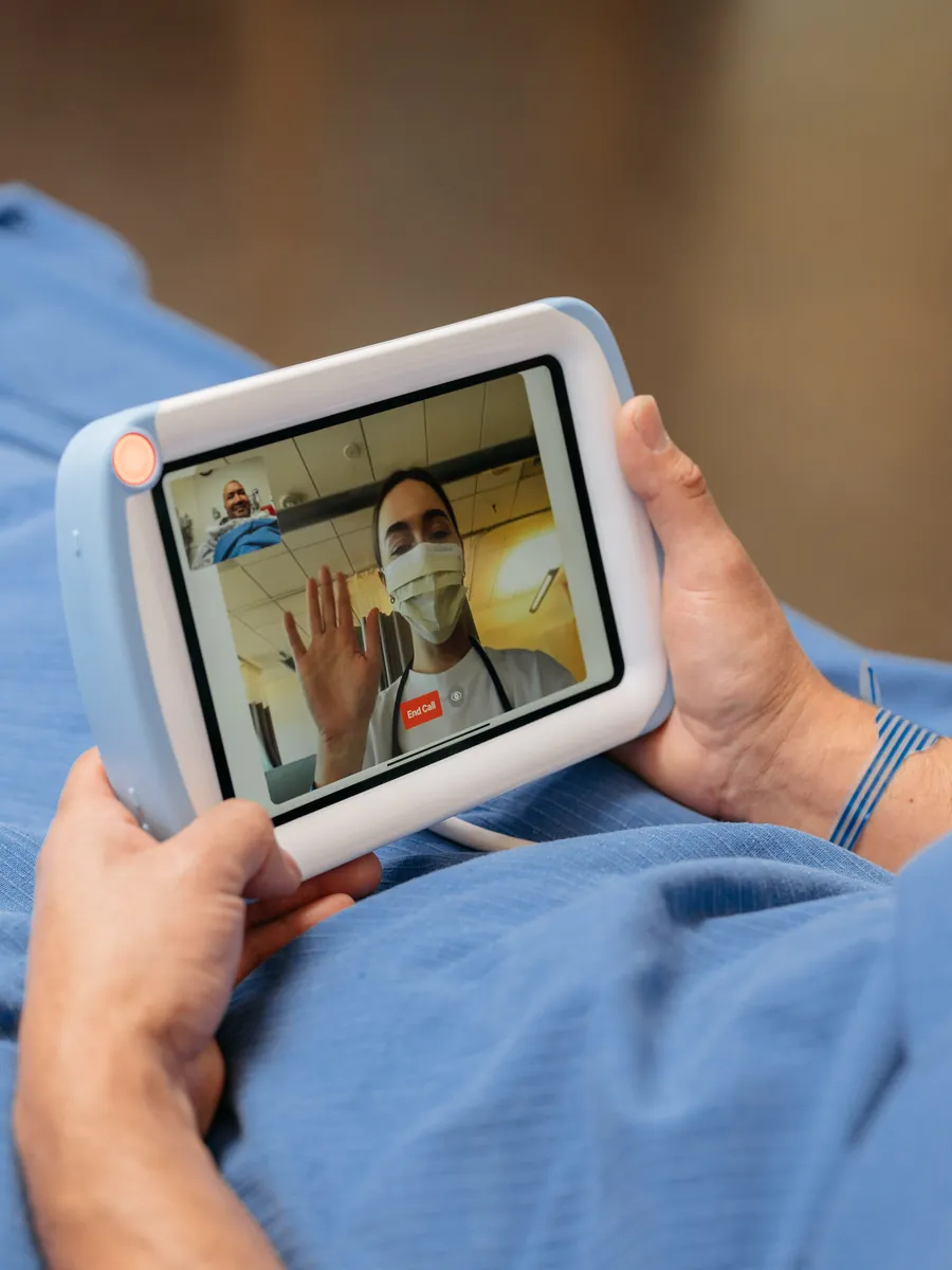A patient waves to a masked nurse on a video call on a PillowCase.