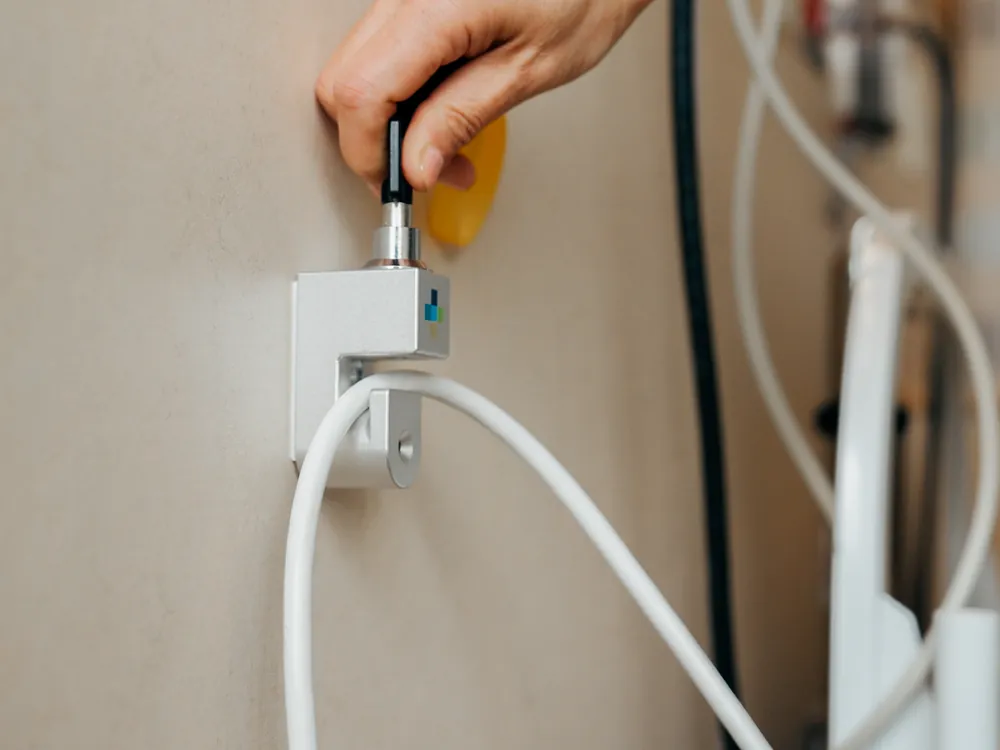 A key turns in the PillowCase cable lock on a hospital wall, the white cable held below it.
