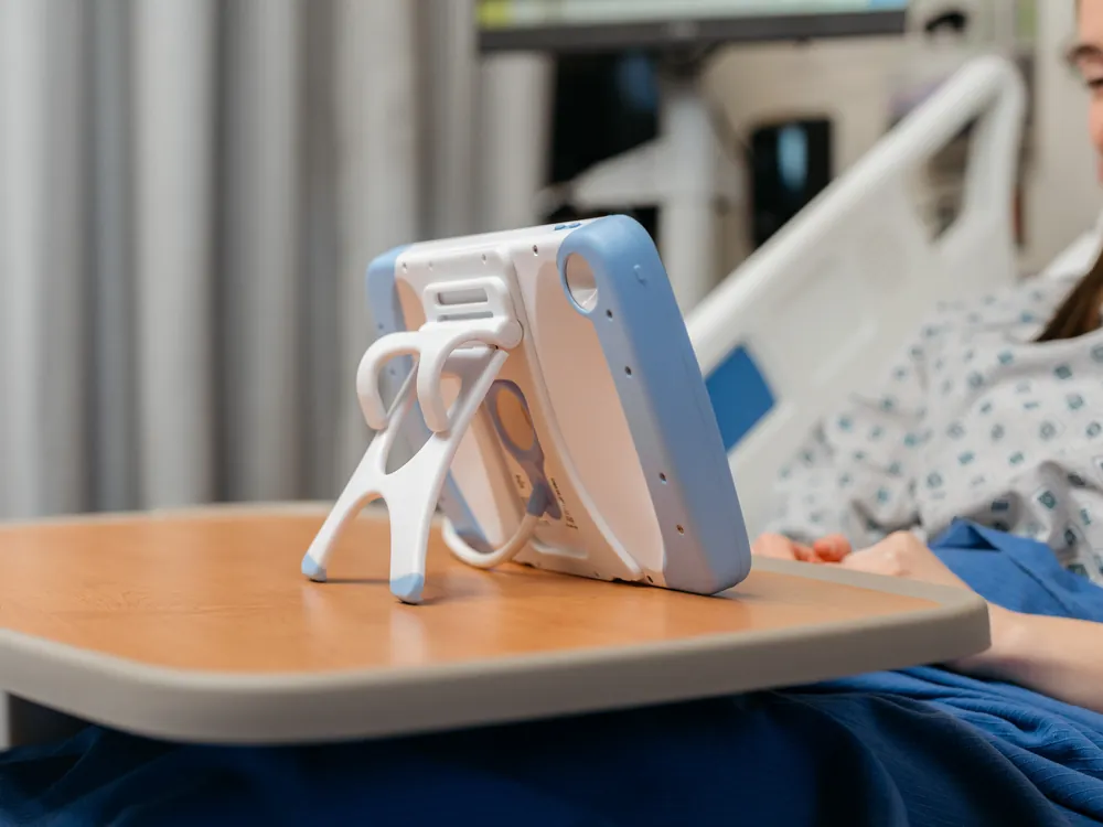 A PillowCase standing on its kickstand on an overbed table beside the bed.