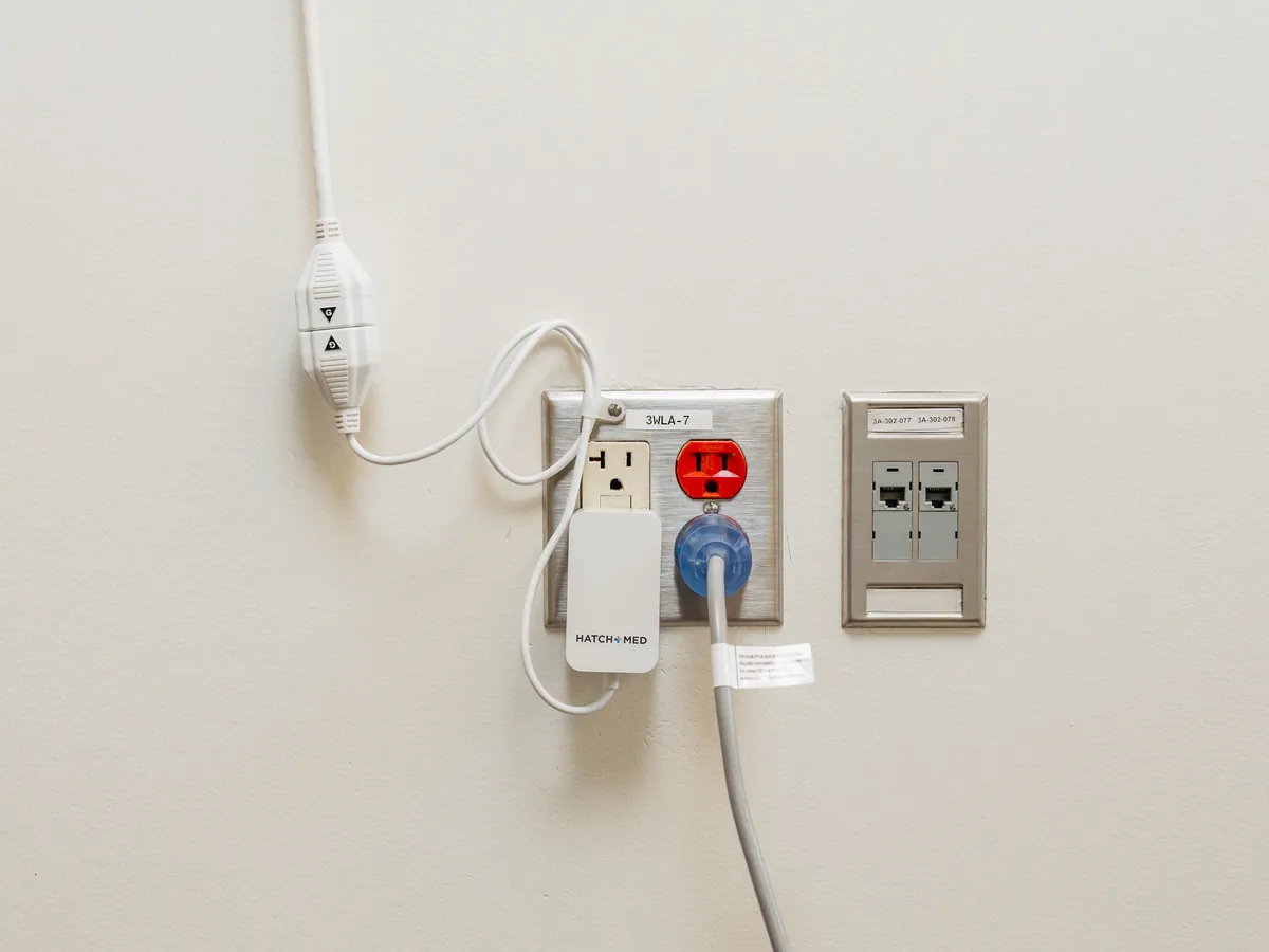The PillowCase power supply in a wall outlet, its magnetic cable clamped to the wall above.
